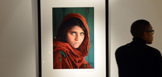 Snímek afghánské dívky v potrhaném červeném šátku a s pronikavýma zelenýma očima.